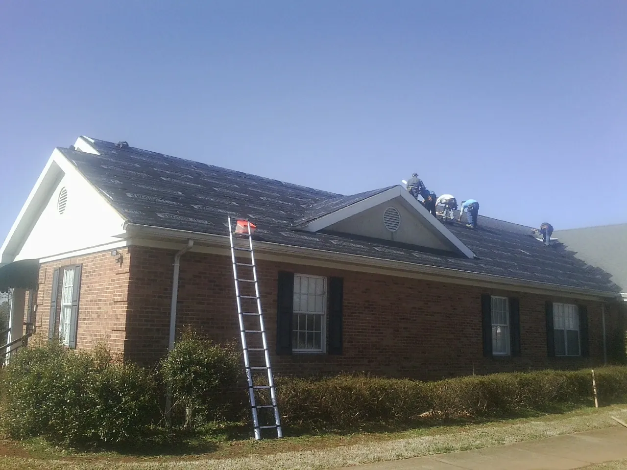 Crew tearing shingles off a brick ranch roof with a ladder set — Emergency Roof Repair work by our crew in Robbins