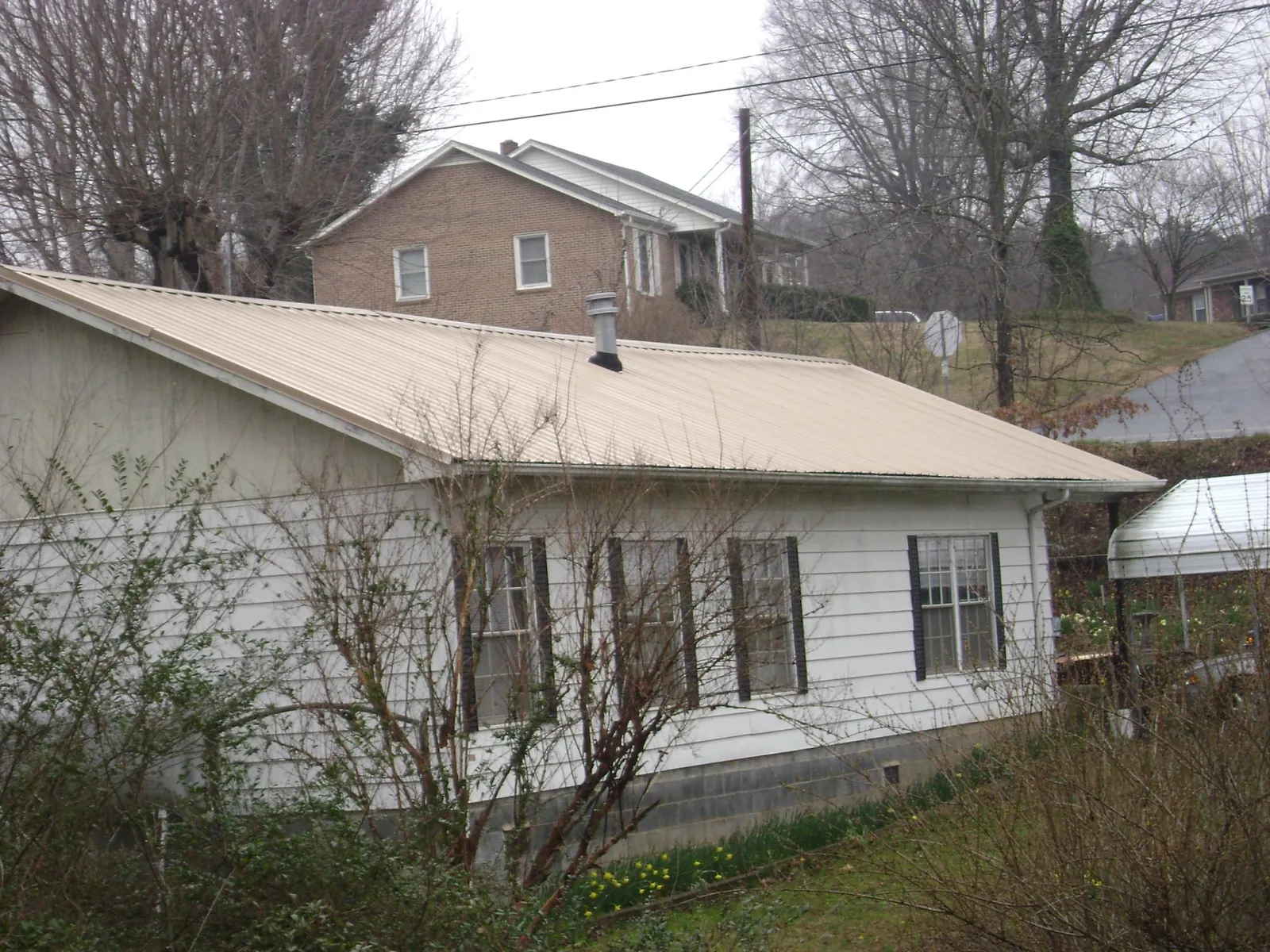 Tan metal roof on a white sided house set into a hillside — Commercial Roofing by Roofing Brothers in Robbins