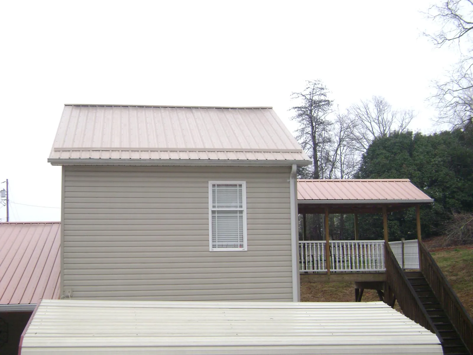 Tan metal roofs on a two story addition and attached porch, from a Roof Replacement job in Robbins